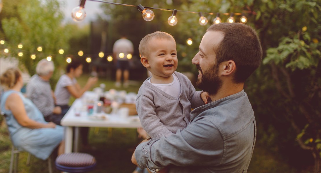 Far med sin son i famnen tittar på varandra och ler i sin trädgård